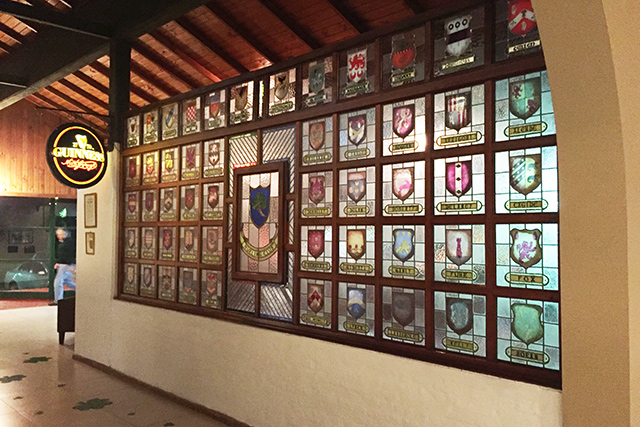 La pared de escudos vitrales del club, cada uno con el apellido de una familia socia.