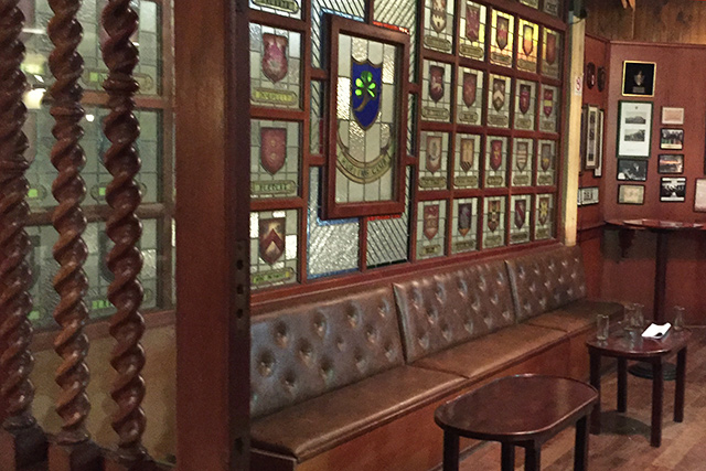 El rincón de los vitrales del club: la pared de escudos en vidriera y los sillones de cuero.